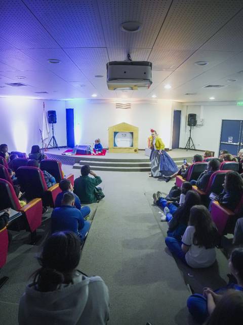 Una sala de conferencias con un público atento y un presentador en el escenario.