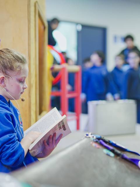 Una niña lee un libro mientras un grupo de niños se prepara para actuar detrás de ella.