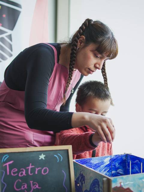 Una mujer con trenzas enseña a un niño a pintar en un taller de teatro.