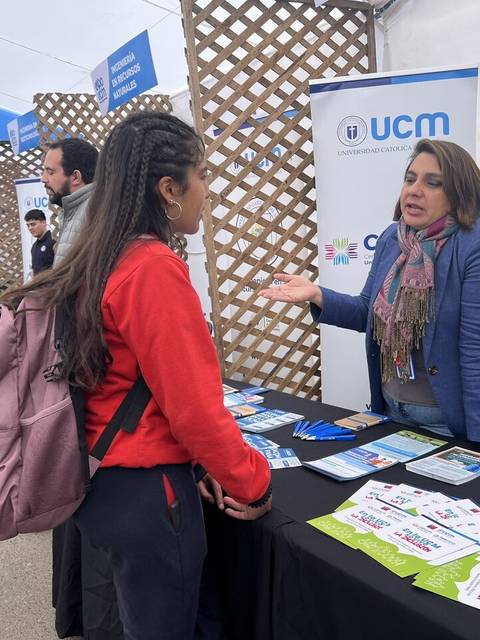 Una persona conversa con una representante de un stand en un evento educativo.