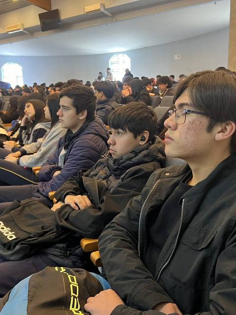 Un grupo de jóvenes sentados en un auditorio prestando atención a una presentación.