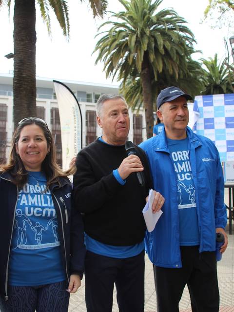 Cuatro personas posan sonrientes en un evento al aire libre con una presentación detrás.