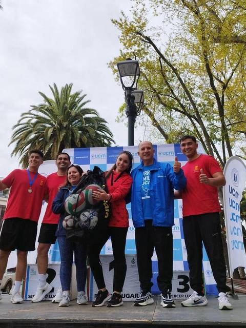 Un grupo de seis personas sonrientes posan en un podio con medallas tras un evento deportivo.