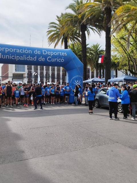 Un evento deportivo se lleva a cabo en las calles de Curicó, con una multitud de participantes y un arco de meta visible.