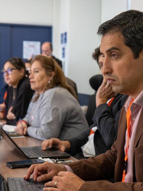 Un grupo de personas está sentado en una sala de reuniones frente a sus computadoras portátiles, participando en una discusión.