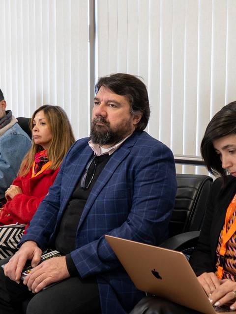 Un grupo de personas sentadas en una sala, algunas con dispositivos electrónicos y otras conversando.