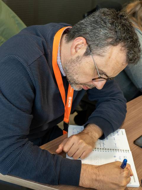 Un hombre con gafas escribe en un cuaderno mientras está sentado en una mesa.