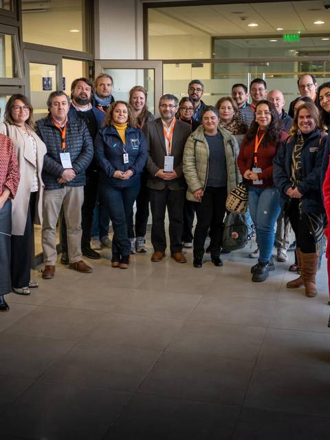 Un grupo de personas posando juntas en un espacio interior, sonriendo y luciendo ropa de trabajo.