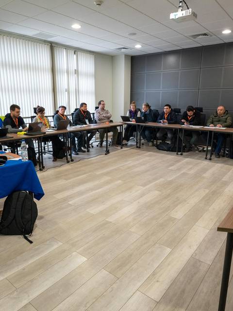 Una reunión en una sala con varias personas sentadas alrededor de mesas.