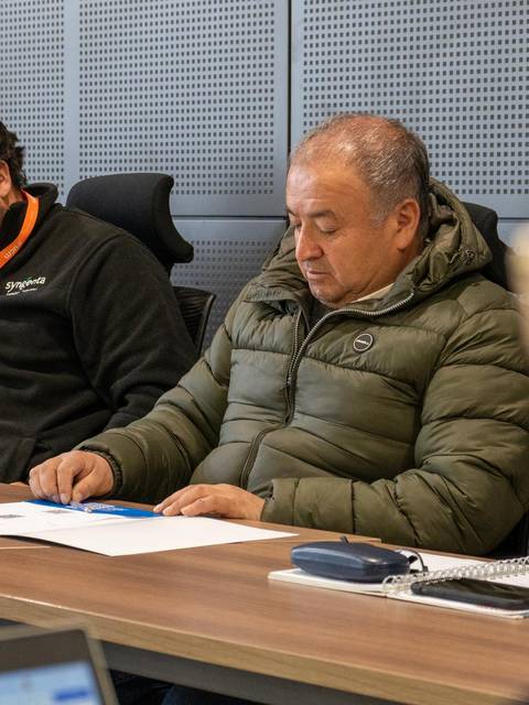 Un grupo de personas se encuentra en una reunión, prestando atención a documentos en una mesa.