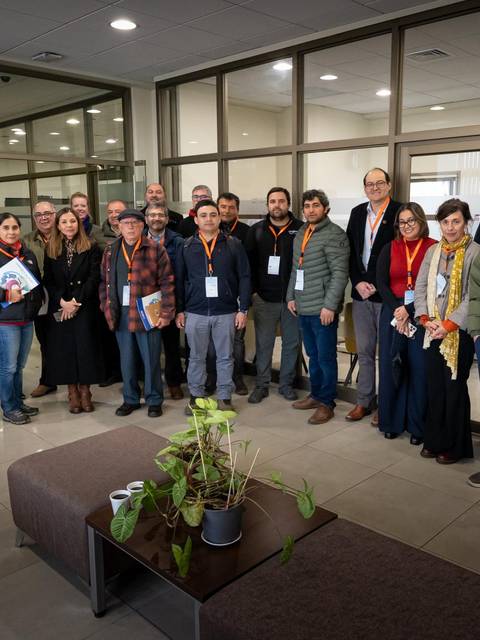 Un grupo de personas posando en un espacio interior con mesas y sillas, algunas de ellas sosteniendo documentos.