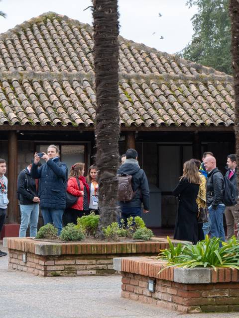 Un grupo de personas conversando frente a un edificio con techado de tejas en un entorno natural.