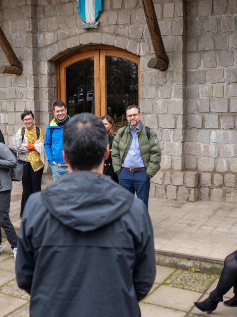 Un grupo de personas conversando en un espacio al aire libre frente a un edificio de piedra.