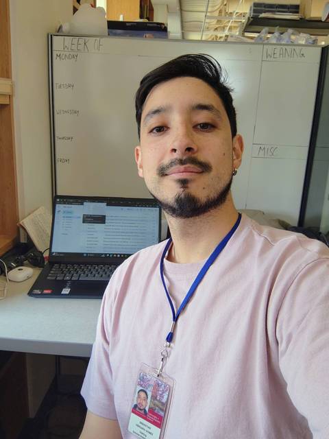 Una persona sonriente se toma una selfie en su lugar de trabajo frente a una computadora portátil.