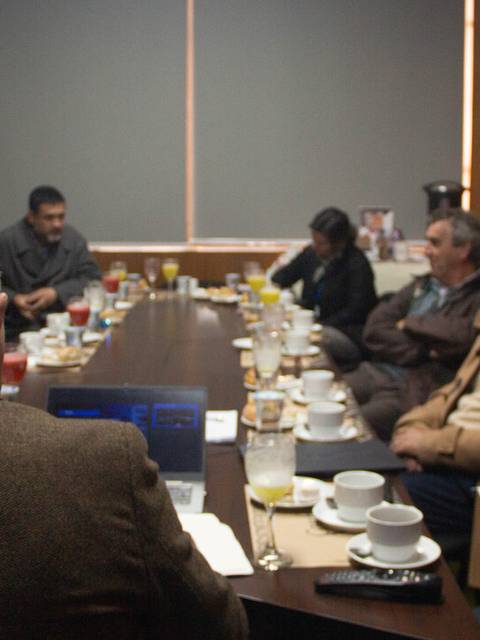 Una reunión de varias personas alrededor de una mesa con café y comida en un ambiente laboral.