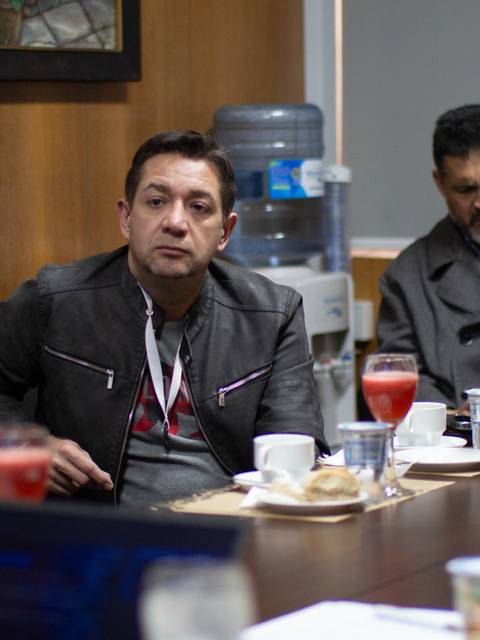 Un grupo de personas se encuentra en una reunión en una sala, con bebidas y bocadillos sobre la mesa.