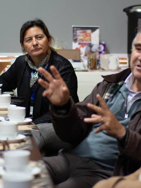 Un grupo de personas participa en una conversación en una reunión alrededor de una mesa con bebidas y comida.