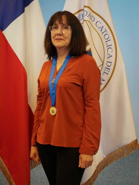 Mujer con medalla y cinta en un acto formal frente a banderas.