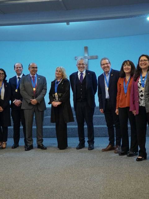 Grupo de personas posando en un evento, mostrando medallas y sonriendo frente a un fondo azul.