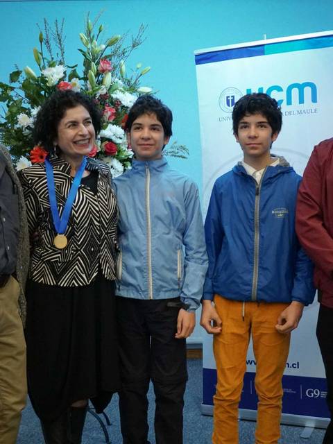 Un grupo de cinco personas posando en un evento con una decoración floral de fondo.