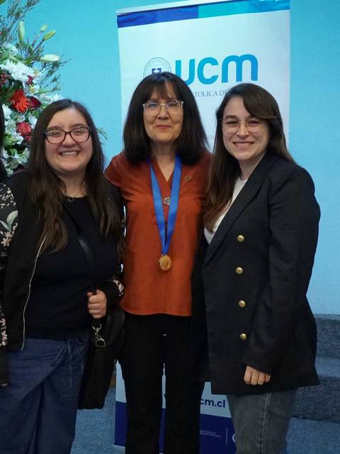 Un grupo de cinco personas posando frente a un fondo decorado con un banner de UCM y flores.
