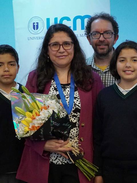 Un grupo de personas sonríe en un evento, mostrando un ramo de flores y rodeados de decoraciones florales.
