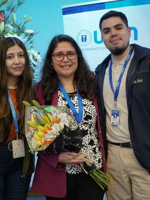 Un grupo de tres personas sonríe mientras sostiene un ramo de flores en un evento.