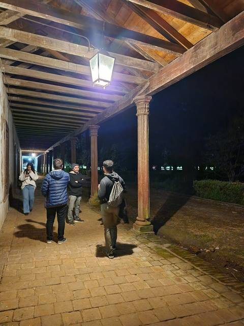 Un grupo de personas conversando bajo un corredor iluminado por faroles en la noche.