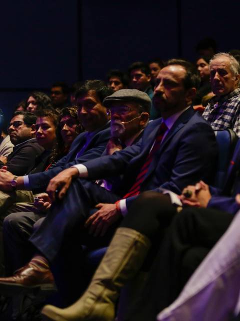 Una audiencia atenta en un evento, con personas sentadas y algunas tomando fotografías.