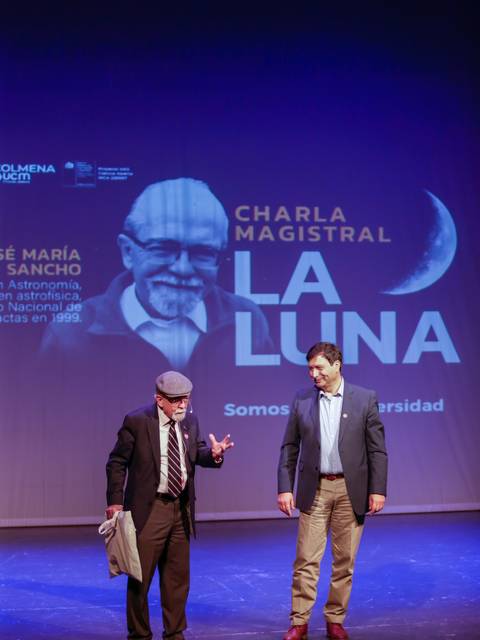 Un evento académico que presenta una charla magistral sobre la luna, con dos oradores en el escenario.