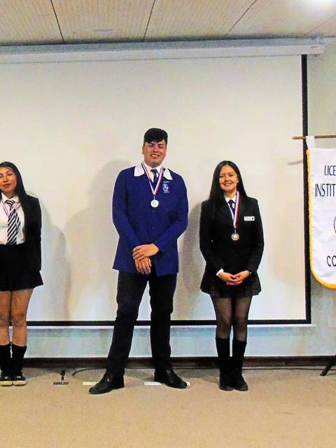 Un grupo de seis personas posando en un evento académico con un presentador y pancartas de fondo.