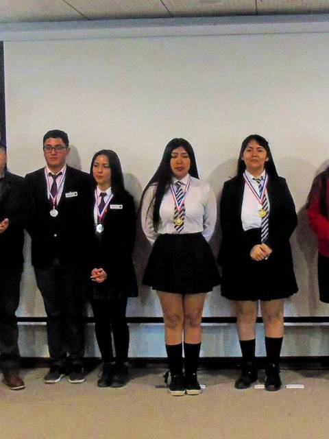 Un grupo de estudiantes con medallas se presenta en un evento formal.