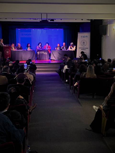 Un auditorio lleno de personas durante un evento con varios panelistas en una mesa.