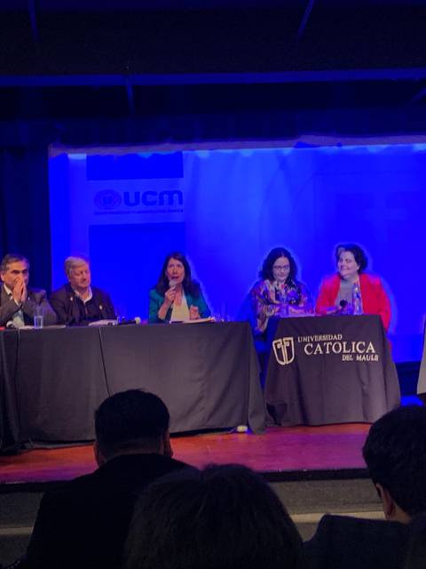 Un panel de discusión en una universidad con varios ponentes sentados detrás de una mesa.