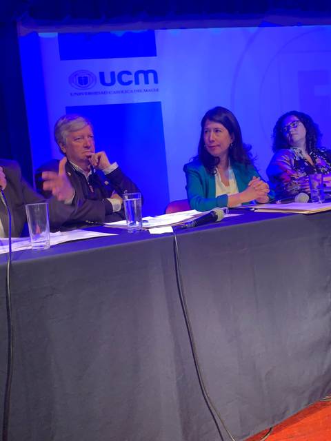 Un panel de discusión con cinco personas sentadas detrás de una mesa, presentando sus ideas en un evento académico.