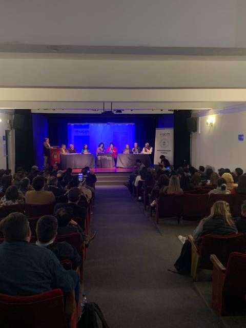 Una conferencia en un auditorio con un gran número de asistentes y un panel de ponentes en el escenario.