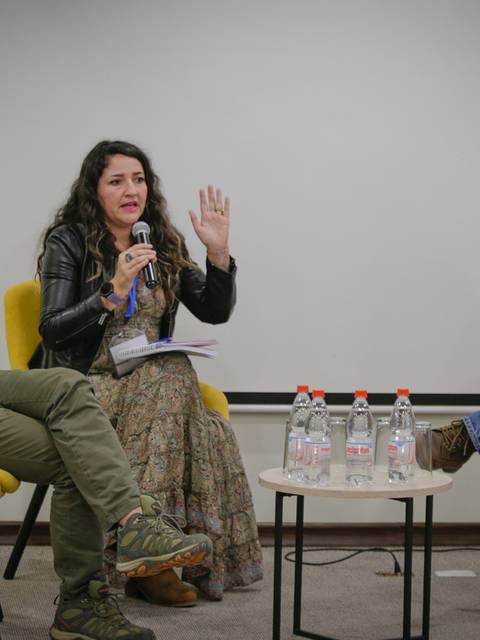Una mujer habla en un panel mientras dos hombres la escuchan atentamente.