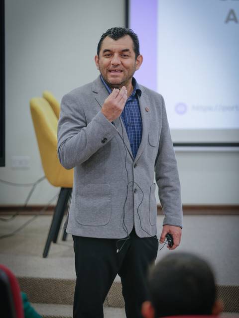 Un hombre se presenta en una conferencia, hablando con entusiasmo mientras sostiene un micrófono.