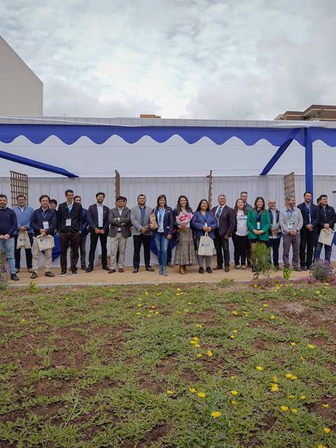 Un grupo diverso de personas posando frente a una carpa en un evento al aire libre.
