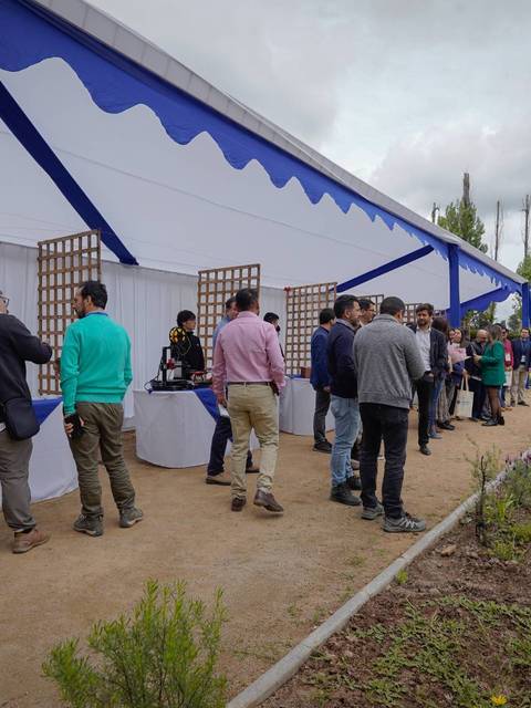 Una feria al aire libre con un toldo y varias personas haciendo fila para visitar diversos stands.