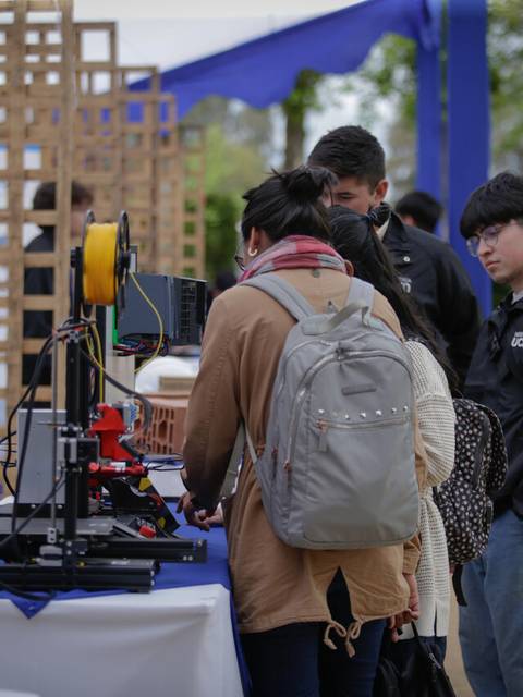 Un grupo de personas observa una impresora 3D en un evento al aire libre.