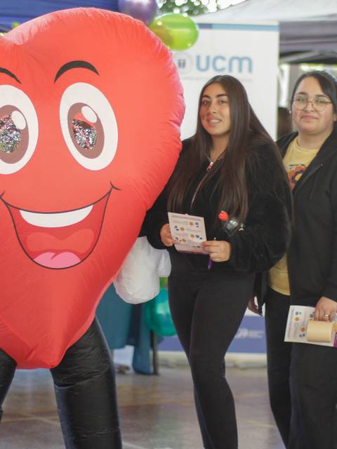 Cuatro personas posan junto a un disfraz inflable de corazón sonriente en un evento.