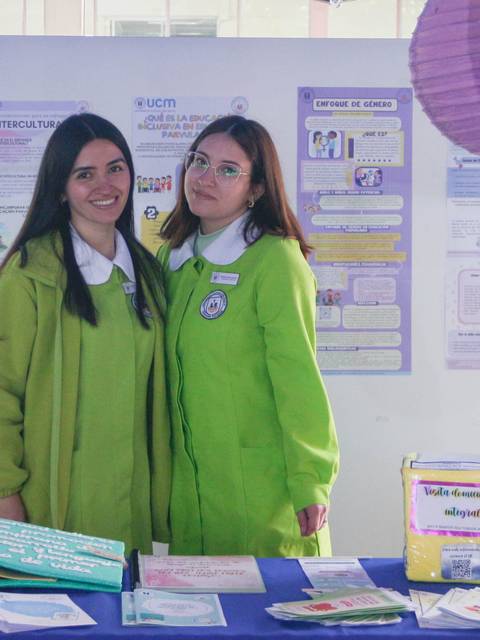 Dos jóvenes posando en un stand decorado con materiales informativos y coloridos.