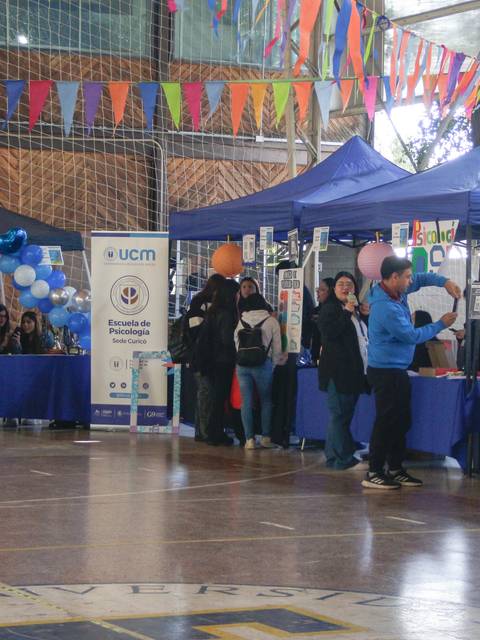 Una feria en un gimnasio con puestos llenos de información y personas interactuando.