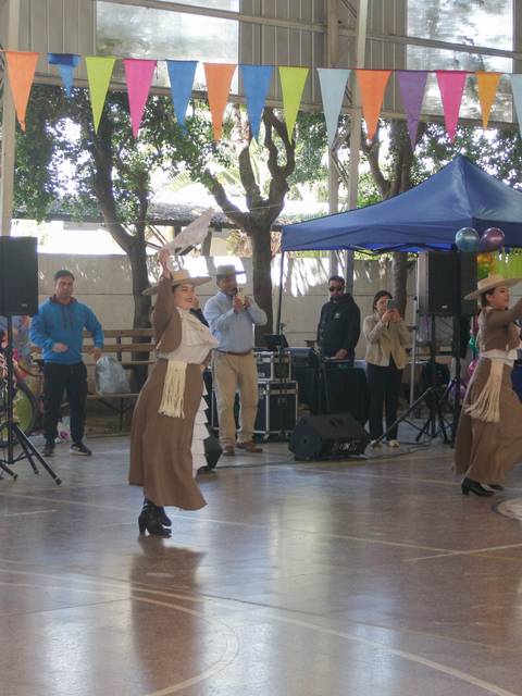 Un grupo de bailarinas en trajes tradicionales danza en un evento festivo bajo coloridos adornos en un gimnasio.