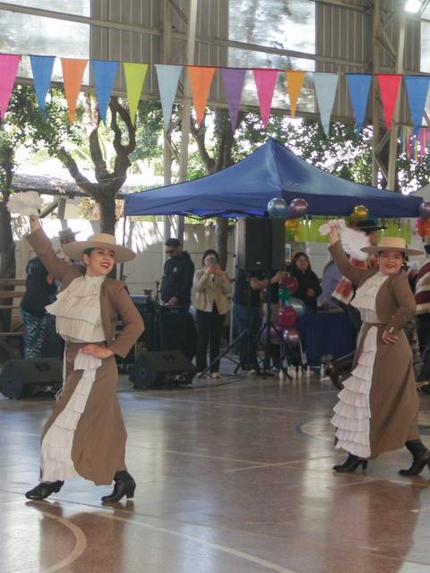 Un grupo de bailarinas realiza una coreografía en un evento festivo bajo una carpa decorada.