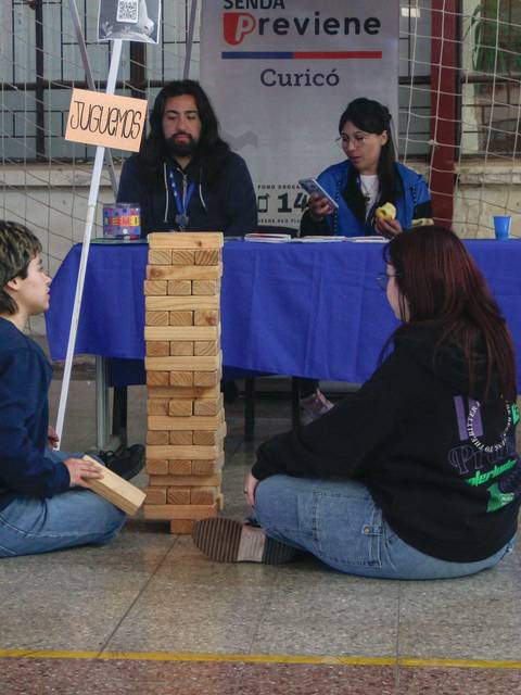 Dos personas están sentadas en el suelo jugando a Jenga en un evento con varias mesas en el fondo.
