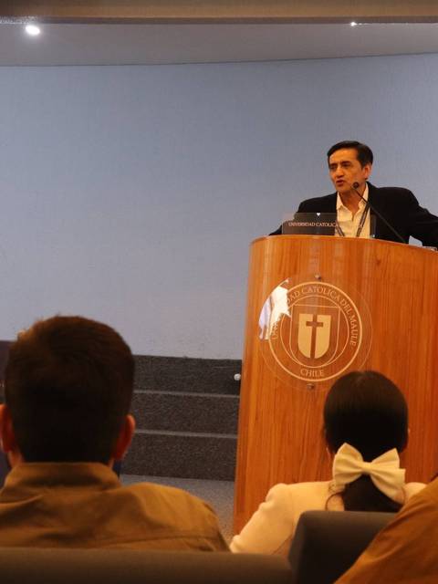 Un ponente habla en una conferencia con una presentación proyectada detrás de él.