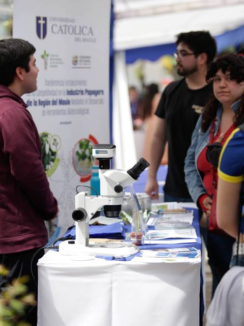 Una feria educativa en la que se exhiben equipos científicos, como un microscopio, mientras los asistentes interactúan y se informan.