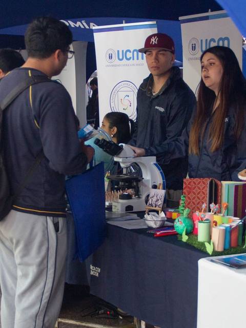 Un grupo de estudiantes interactúa en un evento universitario bajo carpas azules.